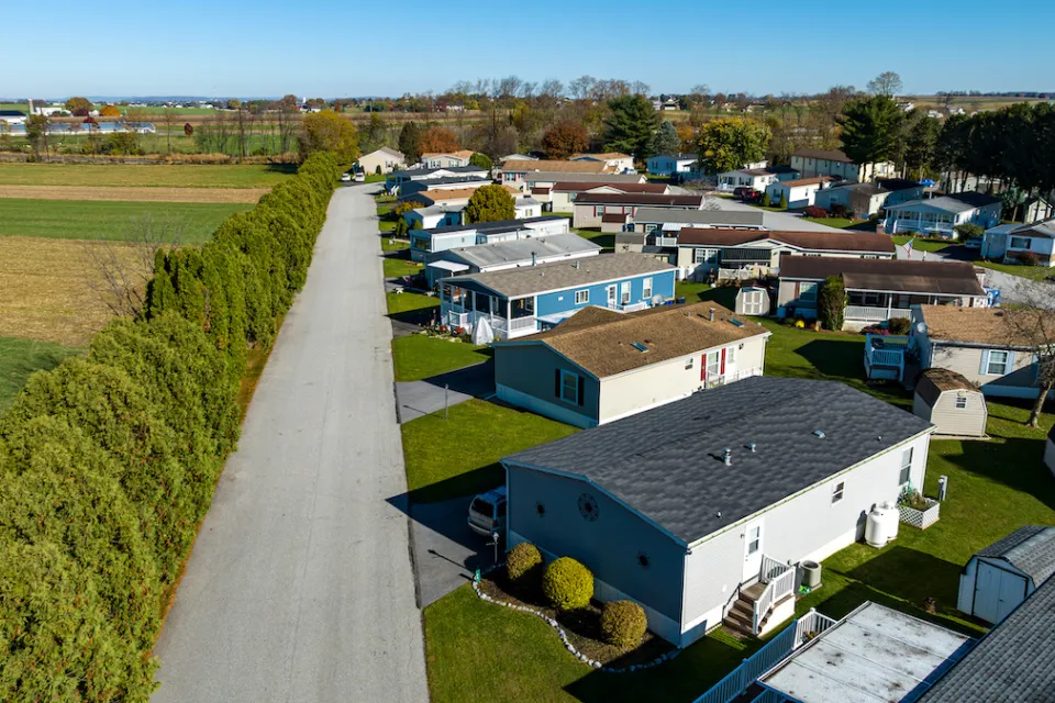 Aerial view of mobile home community in rural area with homes lined up diagonally next to small road.